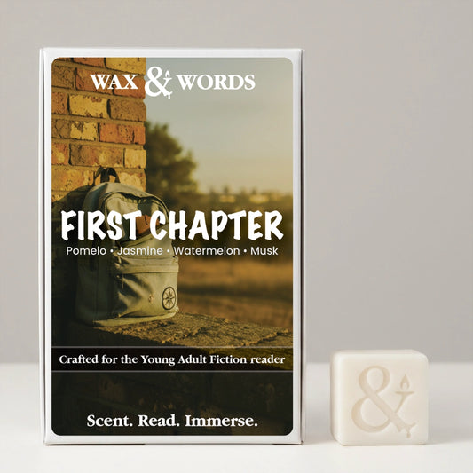 A boxed fragrance product labeled 'Wax & Words' and 'First Chapter' stands upright on a light gray surface, with a small white bar of soap beside it. The box features a warm-toned photo of a backpack against a brick wall and text including 'Pomelo • Jasmine • Watermelon • Musk' and 'Scent.
