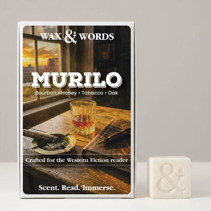 A boxed fragrance product labeled 'Wax & Words Murilo' stands upright on a light gray surface against a light gray background, with a small off-white wax cube beside it. The box front shows a warm-toned scene with a whiskey glass, cigar, and sunset window, and the scent notes 'Bourbon • Honey • Tobacco • Oak.