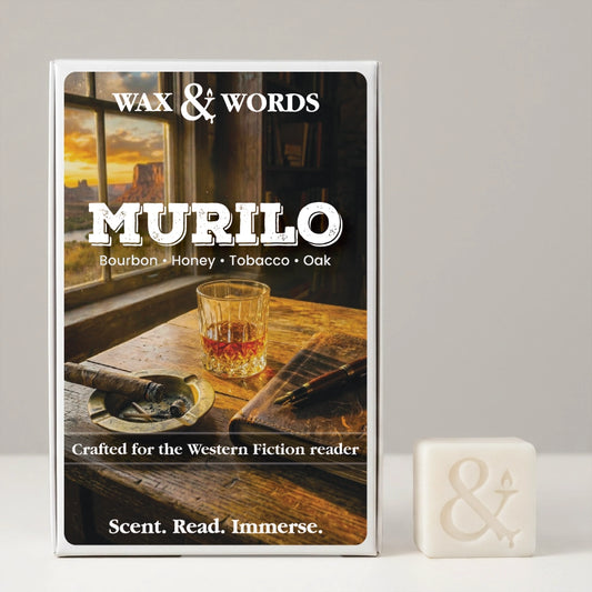 A boxed fragrance product labeled 'Wax & Words Murilo' stands upright on a light gray surface against a light gray background, with a small off-white wax cube beside it. The box front shows a warm-toned scene with a whiskey glass, cigar, and sunset window, and the scent notes 'Bourbon • Honey • Tobacco • Oak.